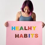 Asian woman holding a colorful 'Healthy Habits' sign in a studio setting, promoting wellness.